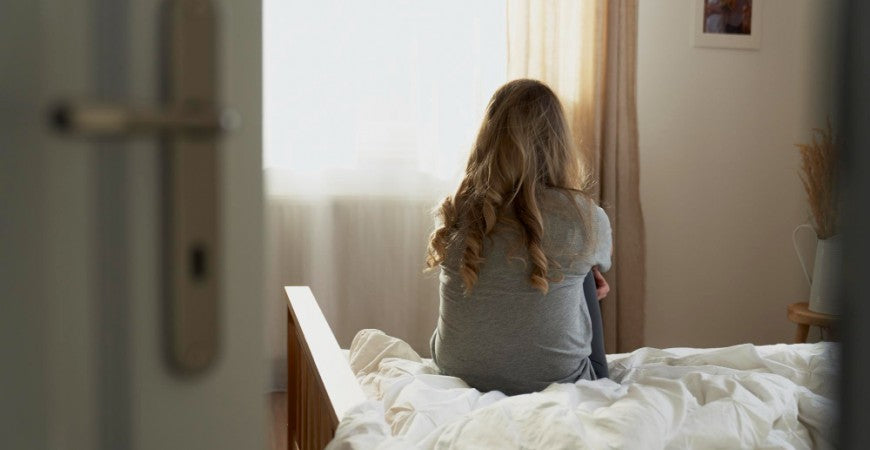Mujer de espaldas sentada encima de la cama