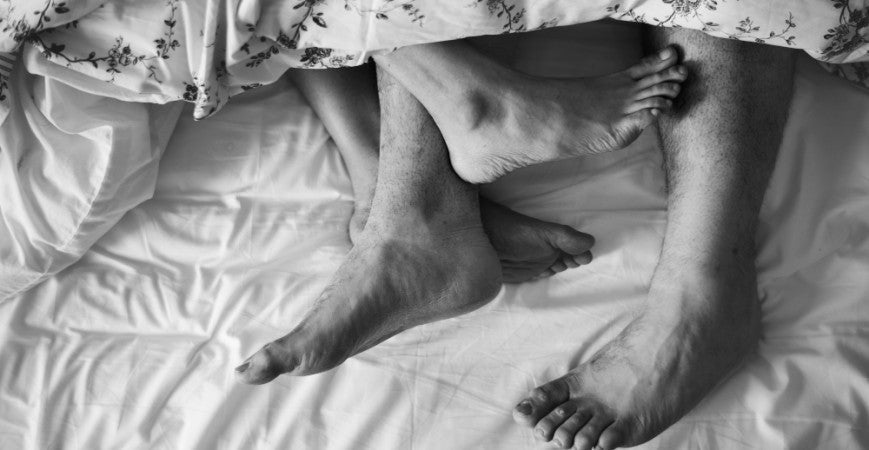 Fotografía en blanco y negro de dos pares de pies enredados en sabanas