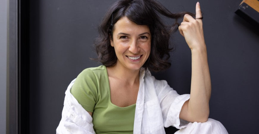 Mujer sonriente sentada, con camiseta verde y camisa blanca
