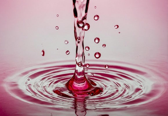 Gota de líquido rosado cayendo sobre agua y formando ondas circulares